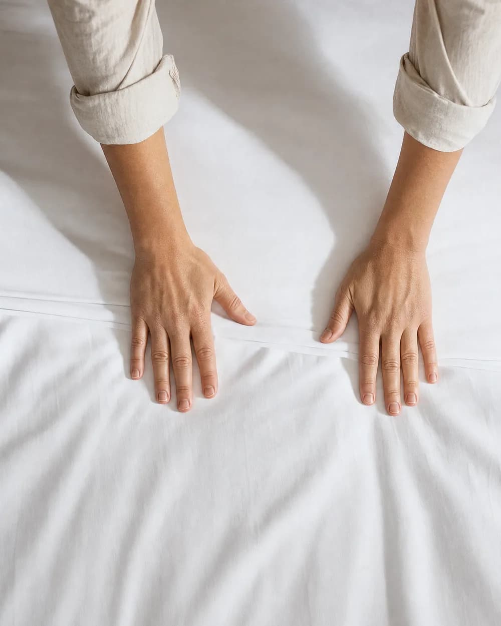 Mains lissant un drap blanc tendu sur un lit : le geste compris dans la commission de 20 %
